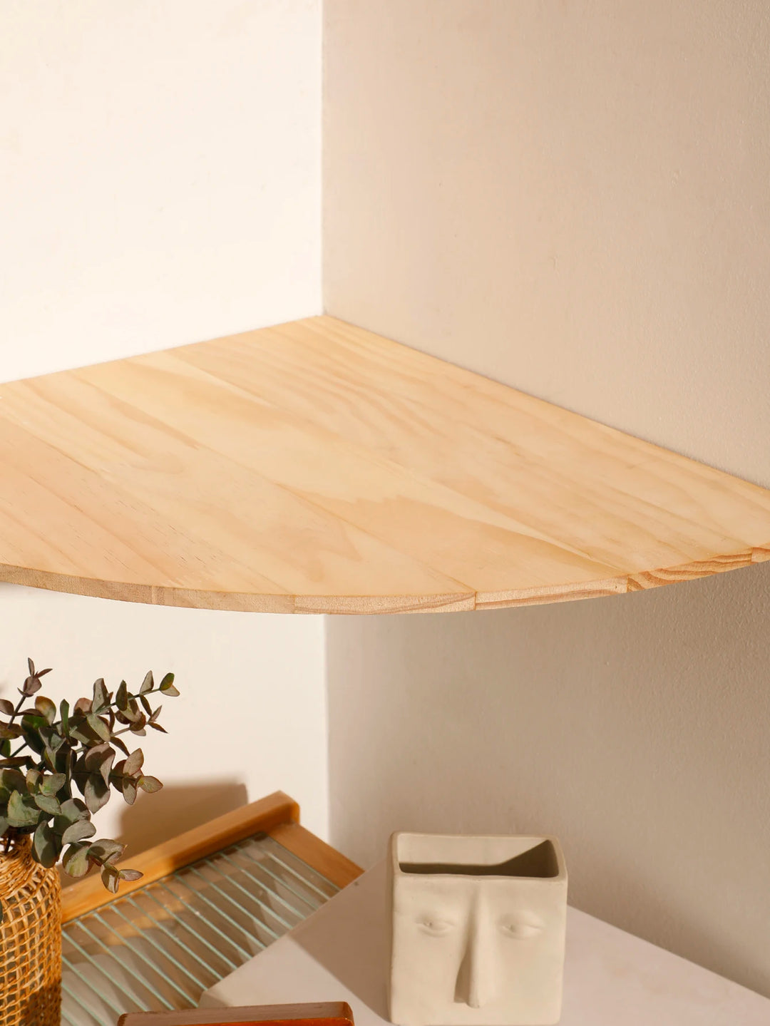 Wooden corner shelf with a plant and decorative items against a neutral wall.
