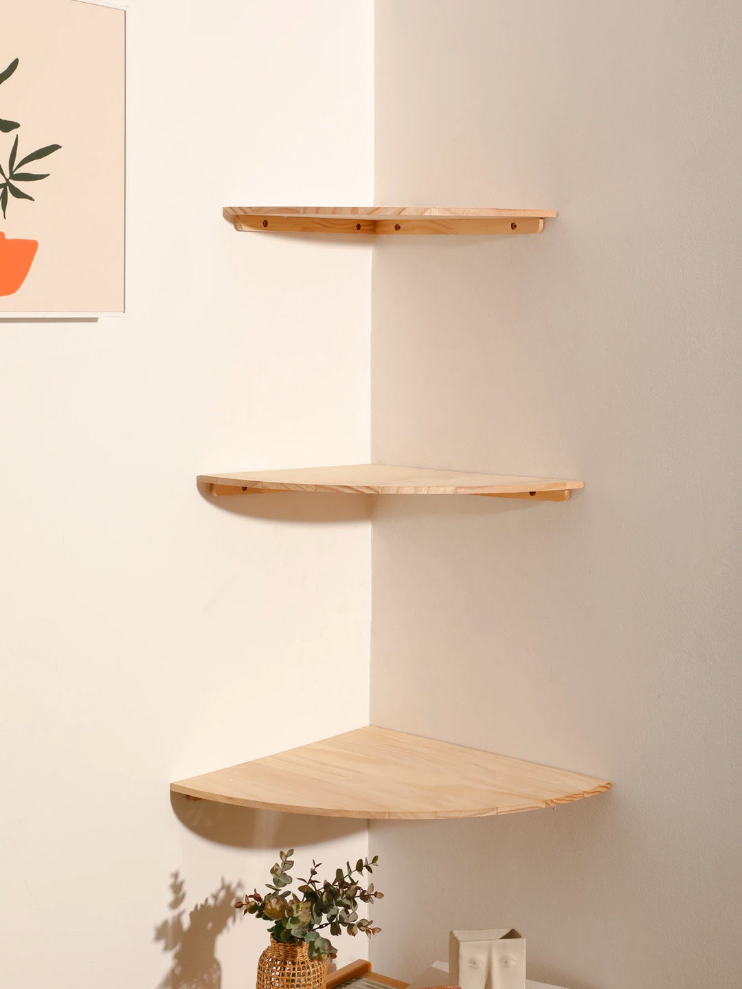 Set of wooden corner shelves against a light wall with a plant on the floor.